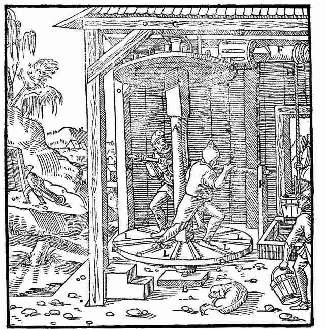 A woodcut: two men on a low turning platform, pushing at its bars to wind a load up from the shaft, while another carries off the buckets.